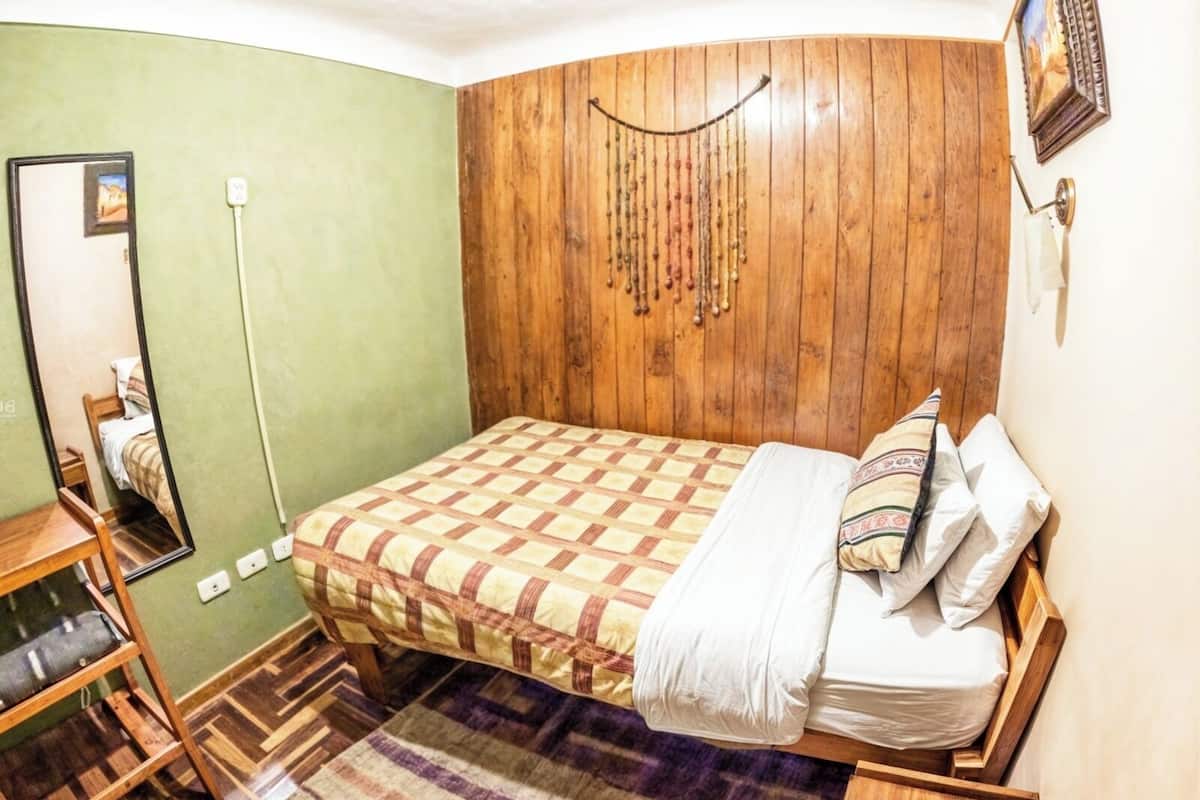 A bedroom with a wooden headboard, a checkered bedspread, a mirror, and a wooden floor.