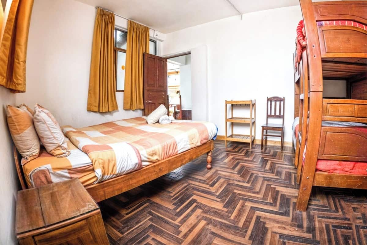 A room with a bed, a wooden bunk bed, a chair, a small table, and a ceiling fan.