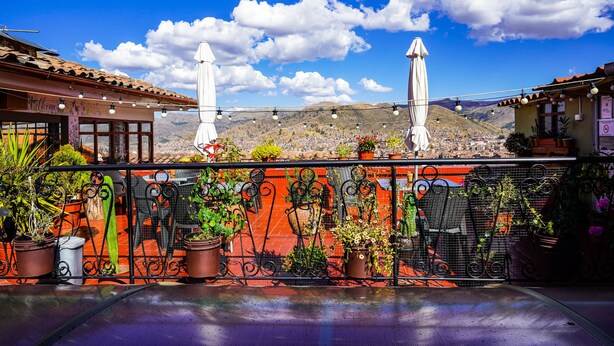 Eine Terrasse mit Topfpflanzen, einem Metallgeländer und Blick auf eine gebirgige Landschaft.