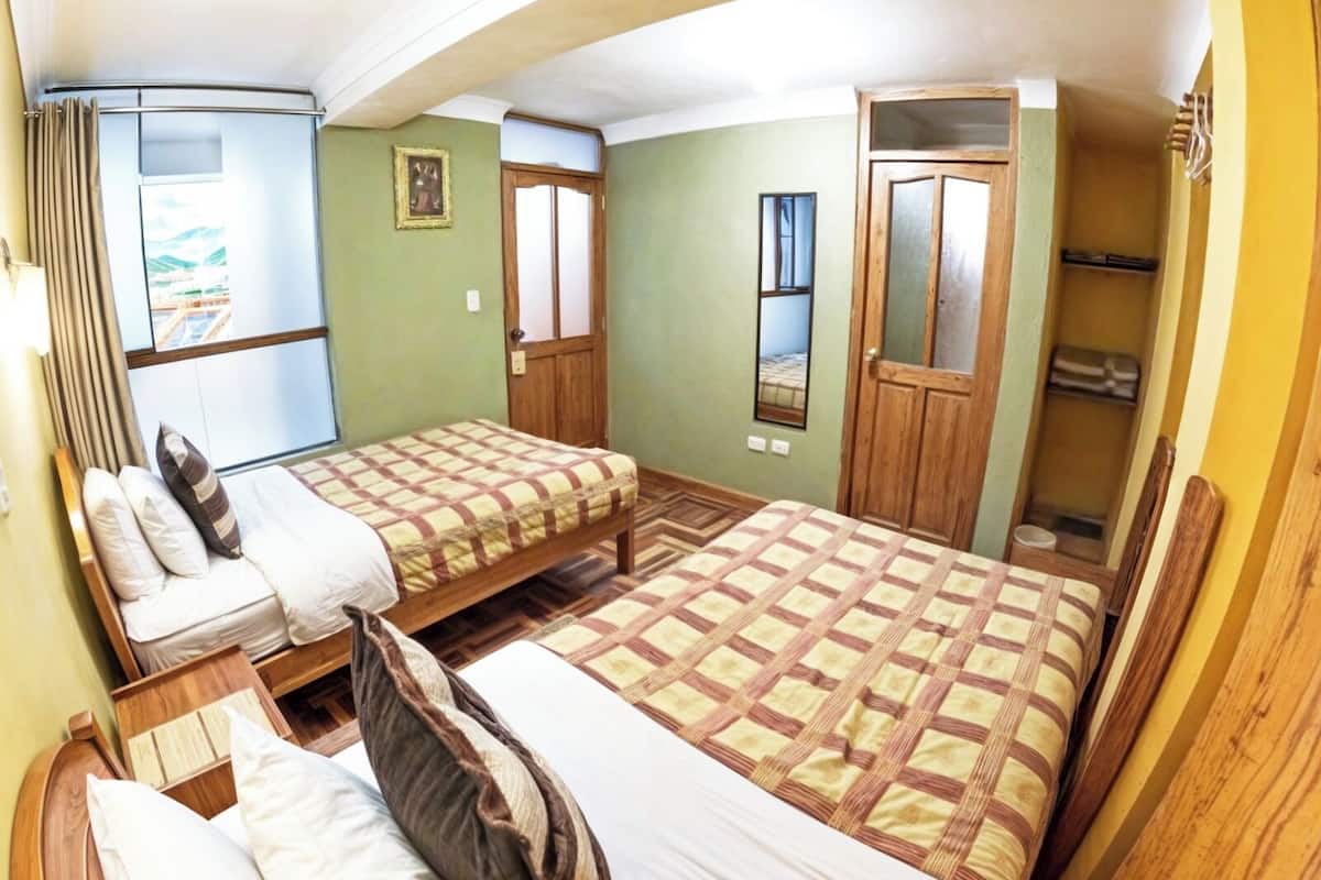 A room with two beds, a wooden wardrobe, a small window, and a door.