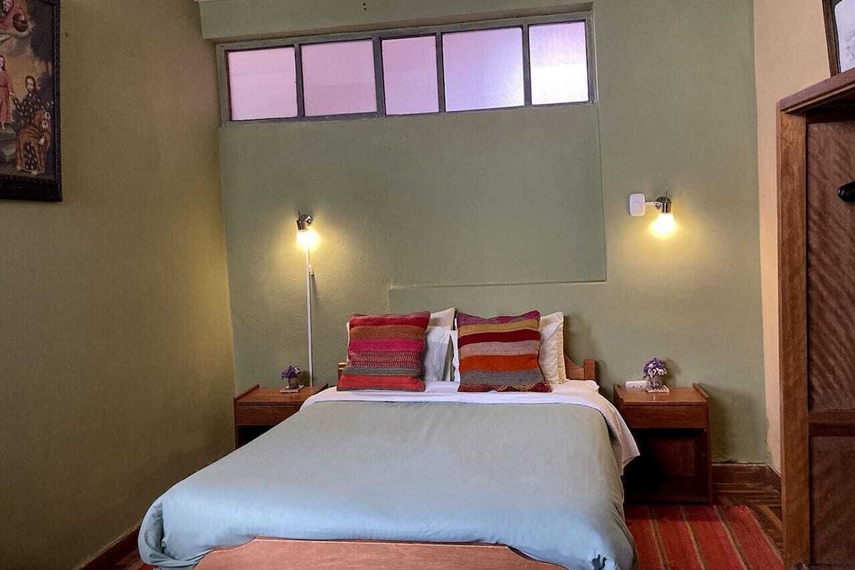 A bedroom with a bed, two bedside tables, a nightstand, a window, and wall-mounted lights.