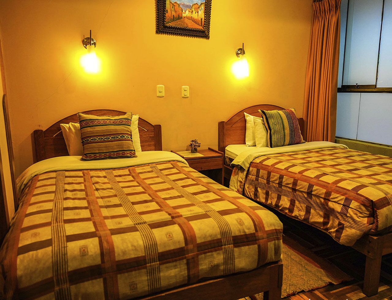 A hotel room with two beds, each with a patterned bedspread, bedside lamps, and a framed picture on the wall.