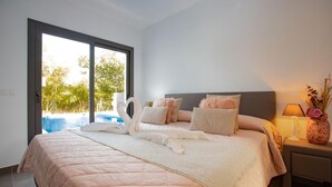 A bedroom with a large bed, a nightstand with a lamp, and a view of a swimming pool through a sliding door. - Villa for rent in Mas Busca, Roses, Costa Brava: Spacious villa with private pool, ideal for families, 3 km from Roses beach. (Roses)