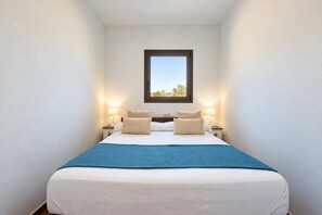A bedroom with a single bed, two bedside lamps, a window, and a view of trees.