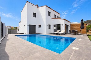 A modern two-story house with a swimming pool, outdoor seating, and a view of the surrounding area.