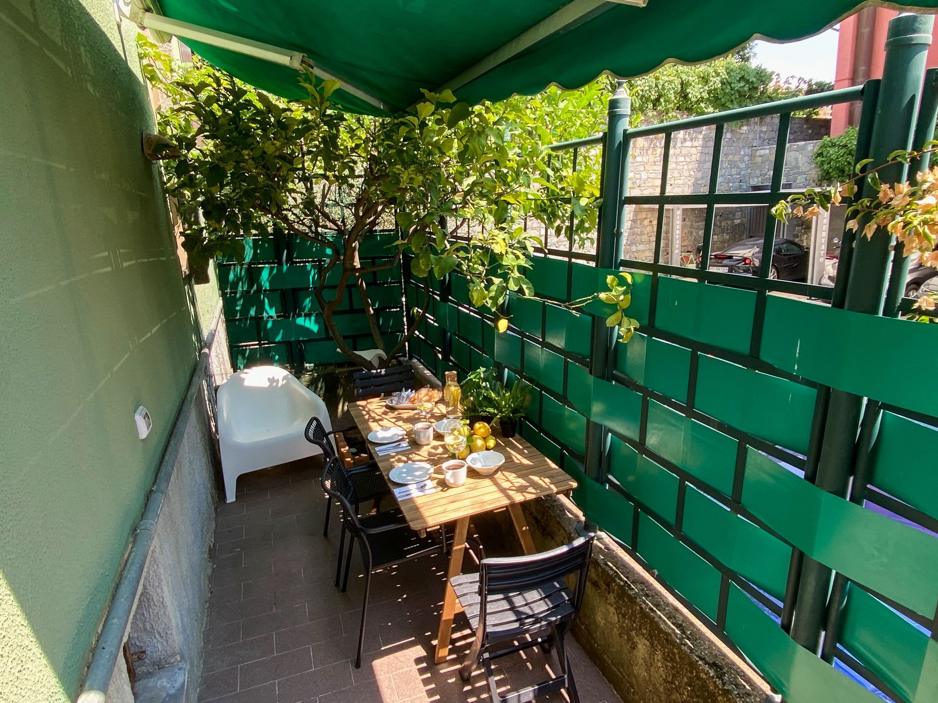 Un espace extérieur aménagé pour prendre les repas, avec une table dressée pour deux personnes, entouré d’une clôture verte et de plantes en pot.