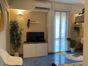 Een moderne woonkamer met een flatscreen televisie, een bank, een eettafel en potplanten.