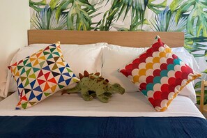 Una cama con cabecera de madera, dos almohadas con diseños geométricos y un peluche de dinosaurio verde.