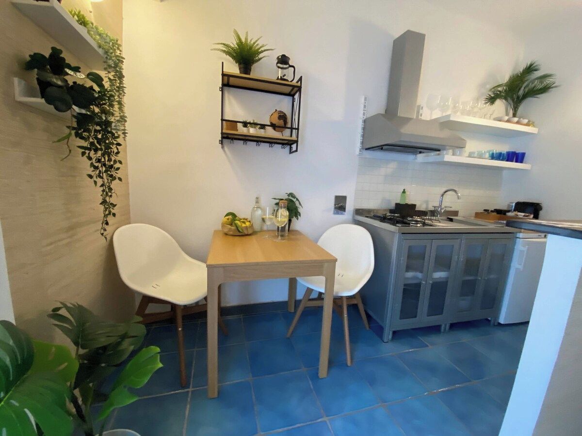 A compact kitchen with a dining area, featuring a wooden table and two chairs, a built-in sink, and a white cabinet.