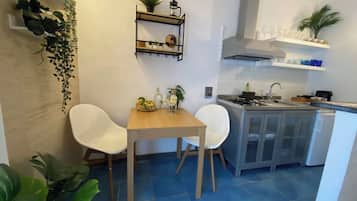 A compact kitchen with a dining area, featuring a wooden table and two chairs, a built-in sink, and a white cabinet.