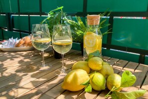 Una mesa con dos vasos de vino blanco, un plato de cruasanes y una botella de limonada con limones.