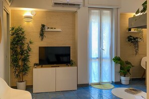 A living room with a flat-screen TV, a sofa, a coffee table, and potted plants.