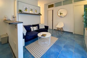 A modern living room with a sofa, a coffee table, and a chair. There is a small shelf with decorative items and a framed picture on the wall.