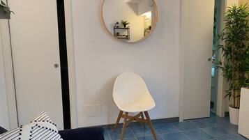 Une pièce avec une chaise blanche, un miroir rond accroché au mur, une plante en pot et un sol carrelé.
