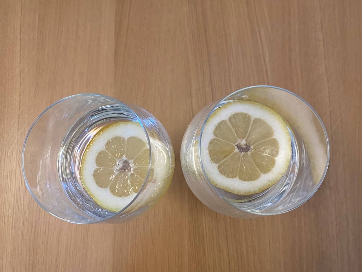 Two glasses of water with lemon slices on a wooden surface.