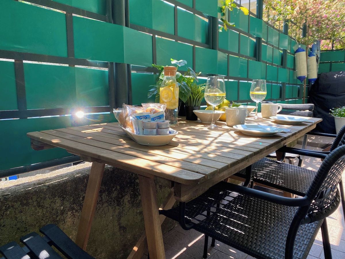 An outdoor wooden table with plates, glasses, and a bottle, set against a green fence.