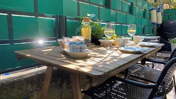 An outdoor wooden table with plates, glasses, and a bottle, set against a green fence.
