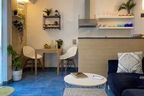 A compact living space with a dining area, a sofa, a coffee table, and a kitchen area with shelves and a stove.