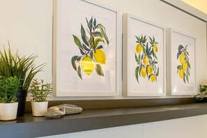 Una pared con tres cuadros enmarcados que muestran limones, una planta en maceta y una pequeña escultura.