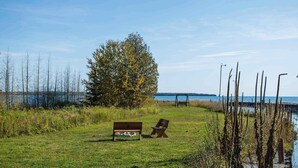 A grassy area with a bench and a chair near a body of water.