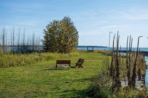 A grassy area with a bench and a chair near a body of water.