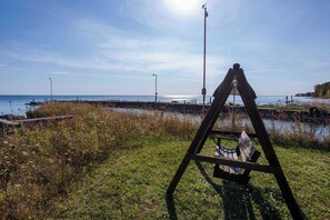 A grassy area with a wooden easel and a bench, a body of water, and a distant pier.