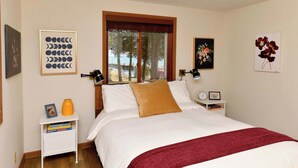 Ein Schlafzimmer mit einem Bett, einem Nachttisch, einem Fenster mit Blick und Wandbildern.