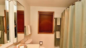 Ein Badezimmer mit Toilette, Waschbecken mit Spiegel, Fenster und Duschvorhang.