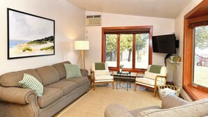 Ein Wohnzimmer mit einer Couch, Sesseln, einem Tisch, einem Fernseher und einem Fenster mit Blick.
