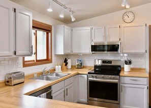 Une cuisine moderne avec des meubles blancs, des appareils en acier inoxydable, un grille-pain et une horloge au mur.