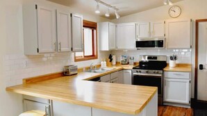 A kitchen with white cabinets, a wooden countertop, a microwave, an oven, and a clock on the wall.