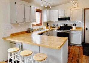 A kitchen with white cabinets, a wooden countertop, a microwave, an oven, and a clock on the wall.