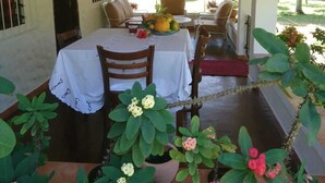 Une terrasse extérieure avec une table dressée pour deux personnes, entourée de chaises, et une structure de plafond en bois.