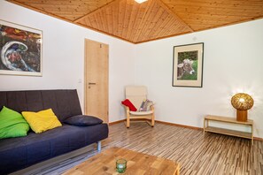 Un salon avec un canapé foncé, une chaise en bois, un tableau encadré, une lampe et un plancher en bois.