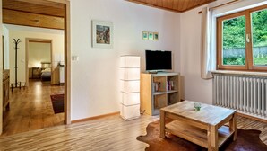 A room with a wooden ceiling, a television on a stand, a window with a view of greenery, and a radiator. - Apartment "Balzerberg" with Garden & Wi-Fi (Weiler-Simmerberg)