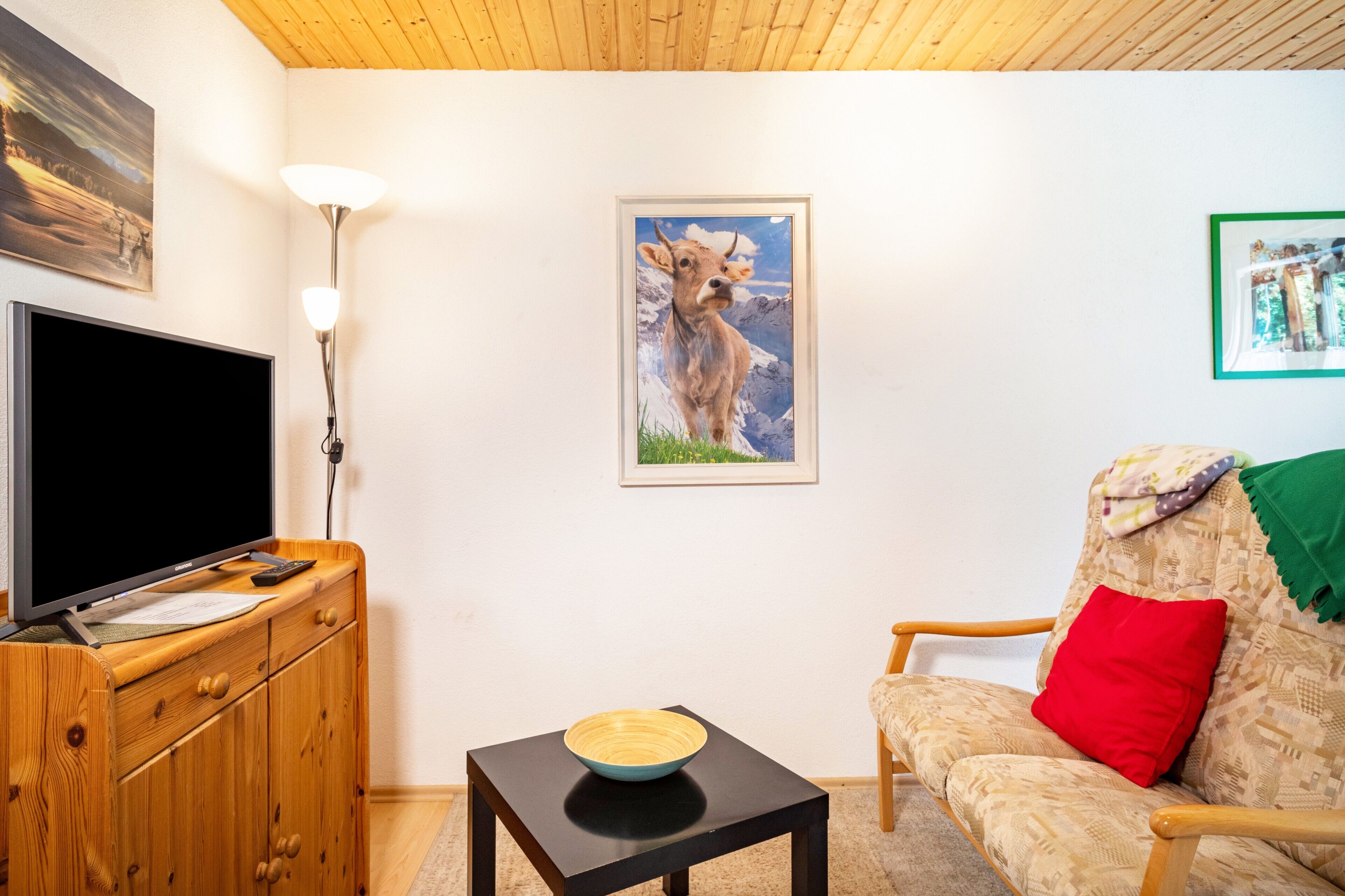 A living room with a television, a framed picture of a cow, a lamp, and a sofa.
