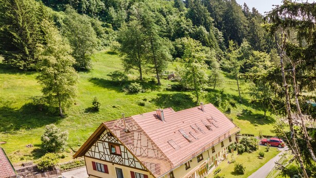 Ein traditionelles Chalet mit Schrägdach, einem Balkon und einer Terrasse mit Gartenmöbeln.