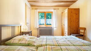 Ein Schlafzimmer mit einem Bett, einem Fenster mit Vorhängen, einem Heizkörper, einem Holzschrank und einem Sessel.