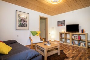 Ein Wohnzimmer mit einer Couch, einem Couchtisch, einem Fernseher, einem Bücherregal und einer Tür.