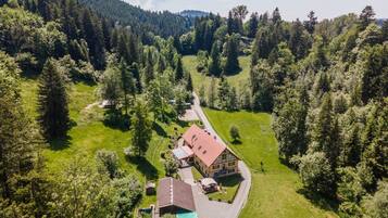 Une grande maison avec un toit rouge, entourée d’un paysage verdoyant et luxuriant et d’une forêt dense.