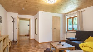 A room with a wooden floor, a sofa with a yellow blanket, a table with a remote control, and a door leading to another room.