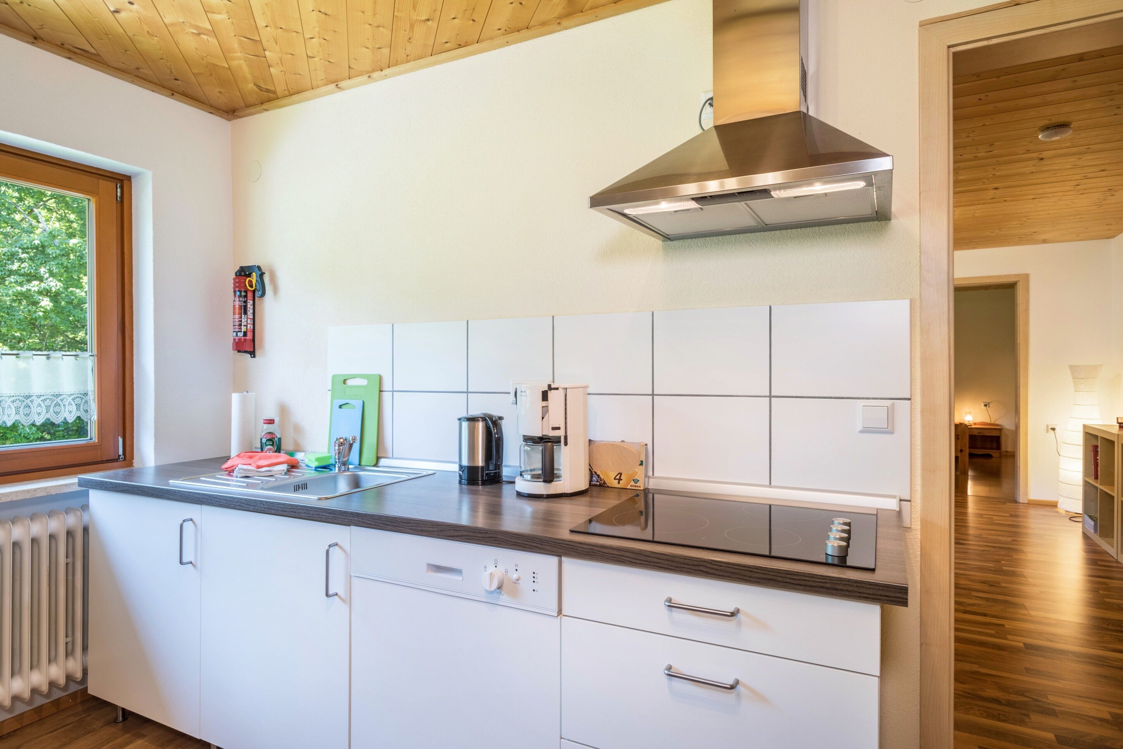 Une cuisine moderne avec des meubles blancs, une hotte en acier inoxydable et une fenêtre donnant sur un paysage verdoyant.