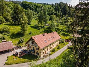 A two-story building with a red roof, surrounded by a green landscape and trees.