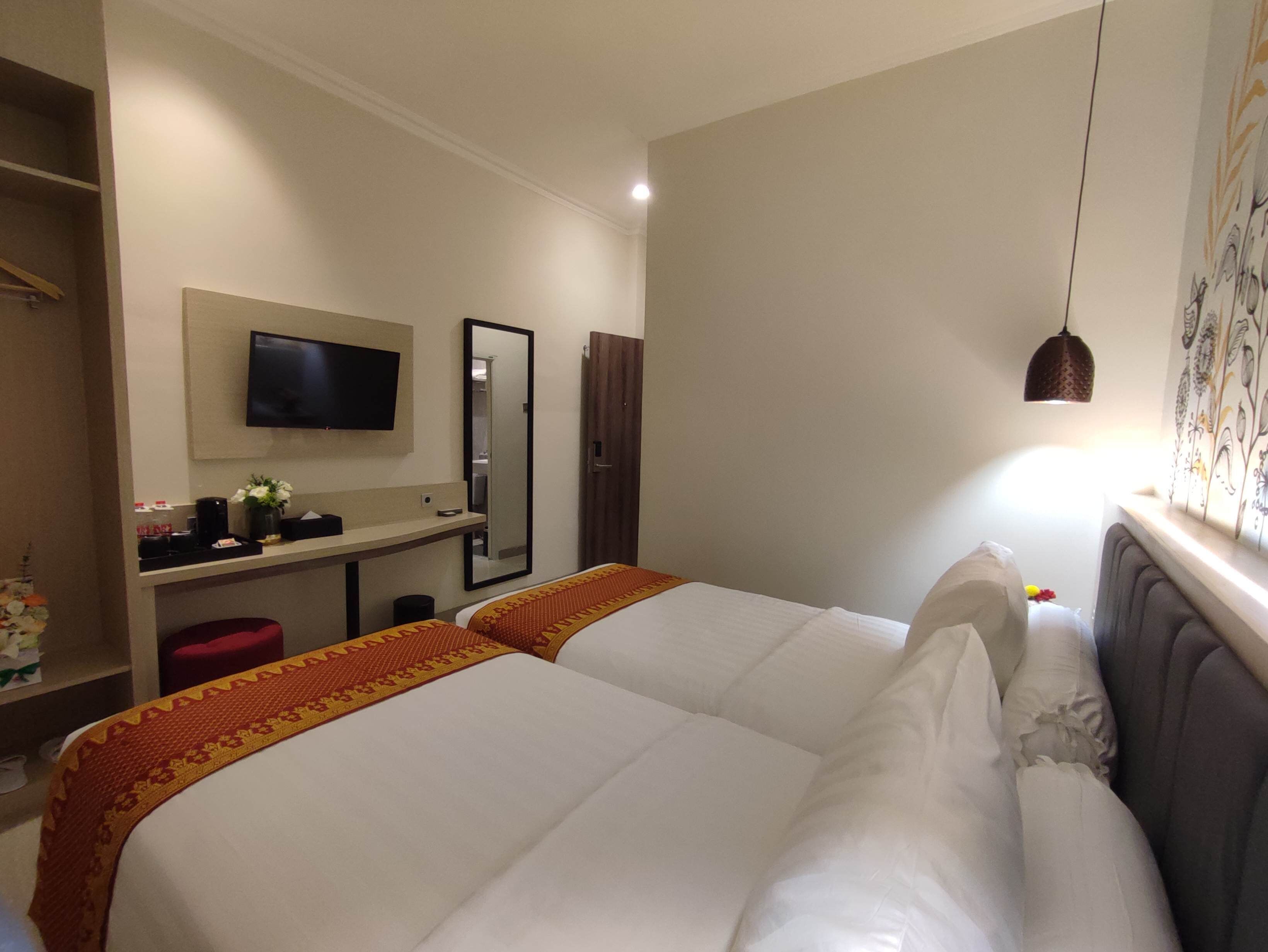 Habitación de hotel con dos camas, televisión, espejo, escritorio y armario.