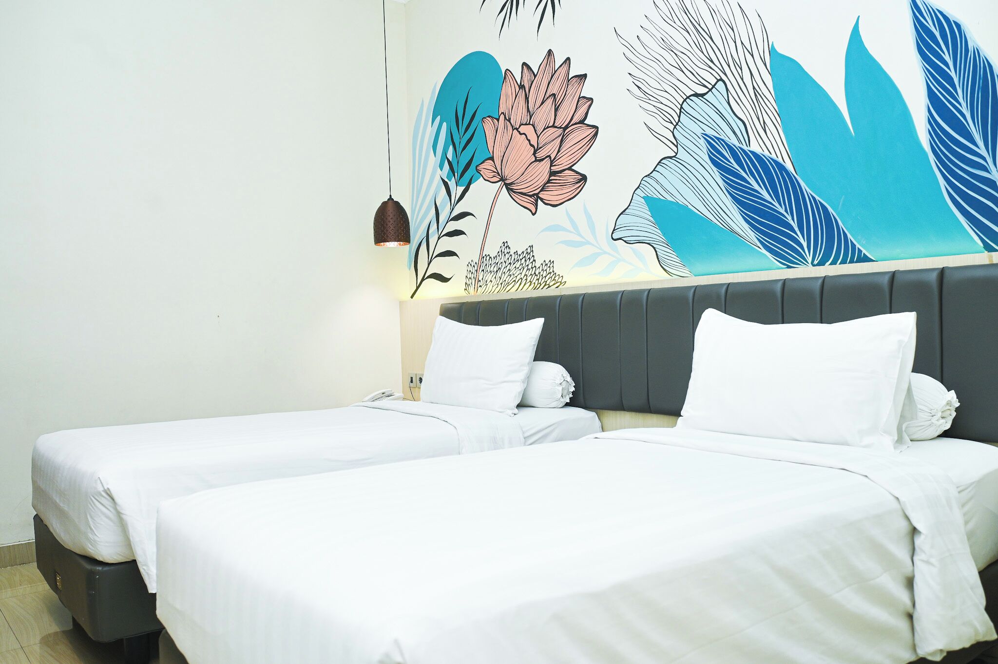 Habitación de hotel con dos camas, cabecero gris y un mural floral y con motivos de hojas.