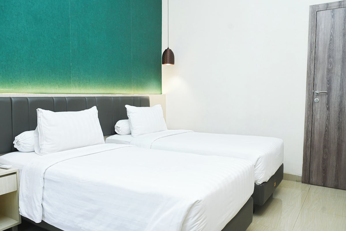 A hotel room with two beds, a green accent wall, a wooden door, and a pendant light.