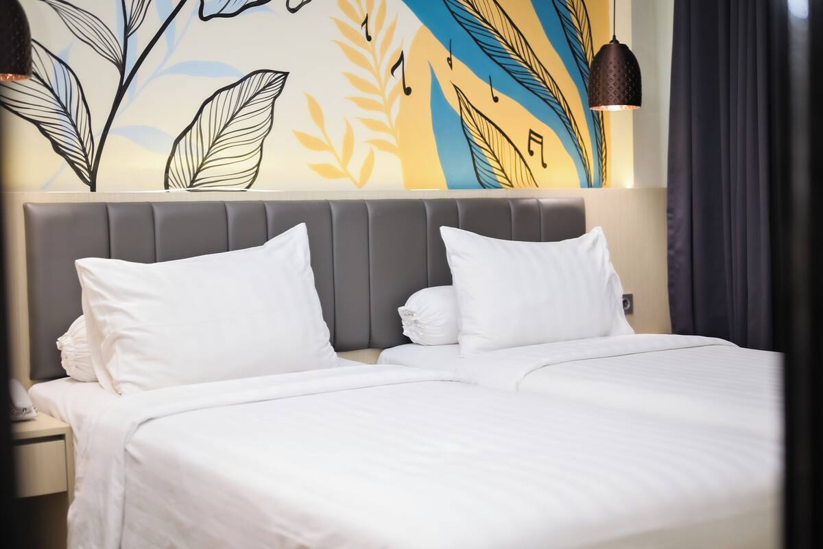 A hotel room with a large bed, two pillows, a grey headboard, and a wall mural with leaf and musical note designs.