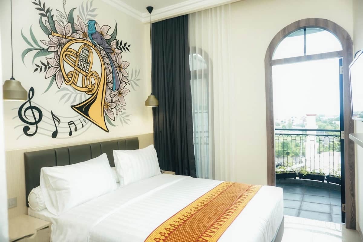 A hotel room with a large bed, a decorative wall mural, a balcony with a view, and a window with curtains.
