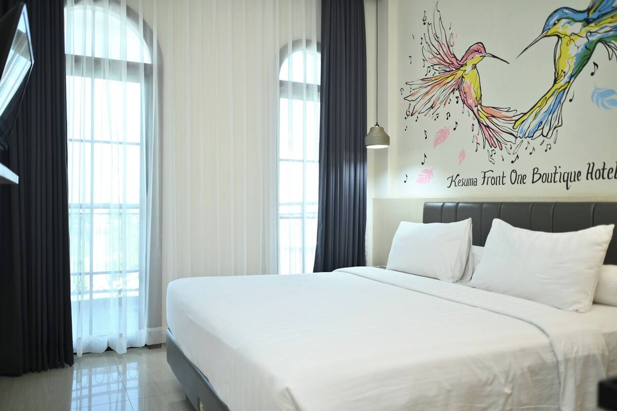 A hotel room with a large bed, a headboard, and a wall mural of birds.