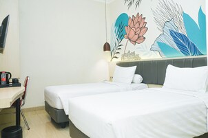 Habitación de hotel con dos camas individuales, un escritorio con silla, cafetera y un mural floral y con motivos de hojas.
